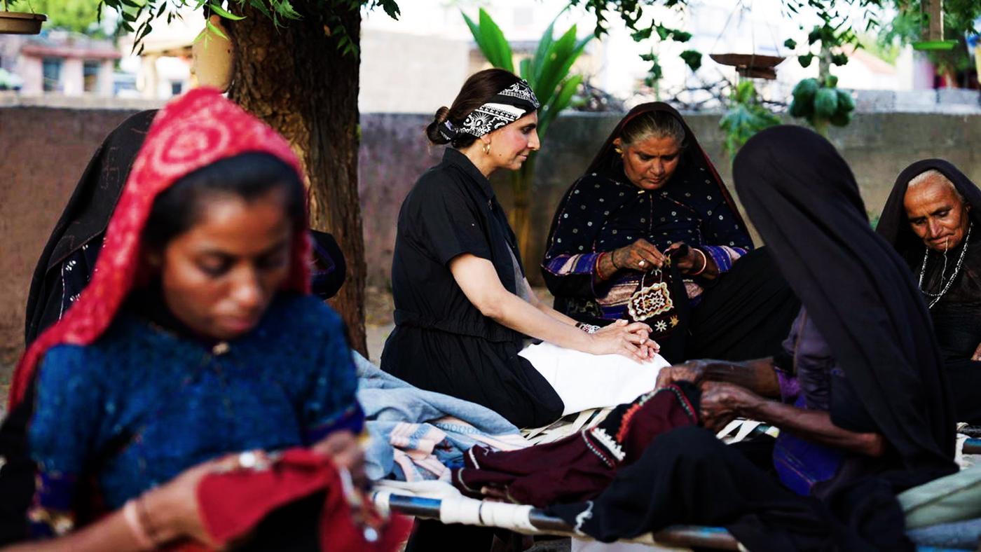 A designer sitting with artisans at a craft pocket, working on a piece together outdoors